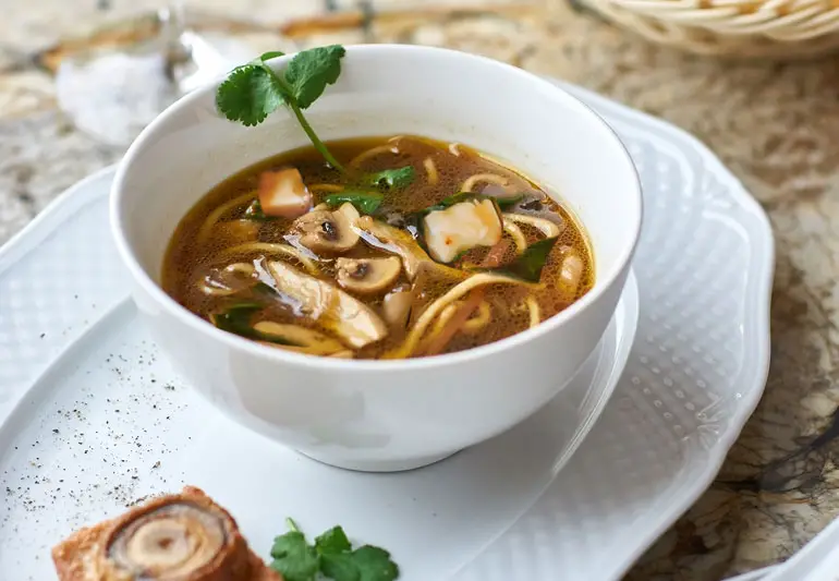 Balta bļoda ar soba tofu un spinātu nūdeļu zupu, kas dekorēta ar cilantro